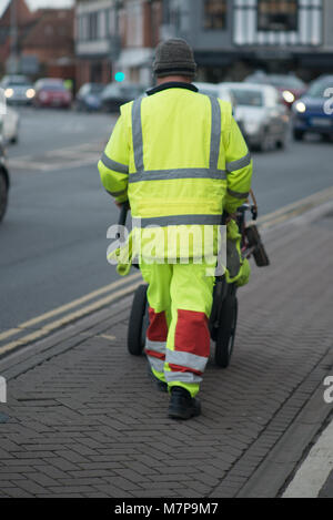 Street Sweeper geht weg drücken Ref und grau Barrow mit dem Gebäude im Hintergrund Stockfoto