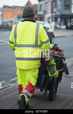 Street Sweeper geht weg drücken Ref und grau Barrow mit dem Gebäude im Hintergrund Stockfoto