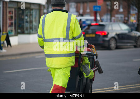 Street Sweeper geht weg drücken Ref und grau Barrow mit dem Gebäude im Hintergrund Stockfoto