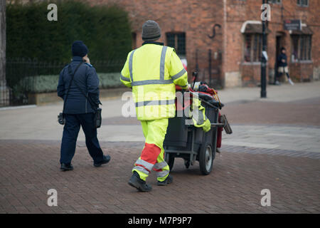 Street Sweeper geht weg drücken Ref und grau Barrow mit dem Gebäude im Hintergrund Stockfoto