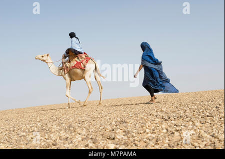 Frau Fuß hinter einem Mann reiten auf einem Kamel in Mauretanien, Westsahara Wüste. Stockfoto