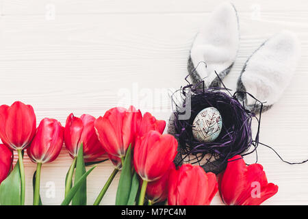 Hasenohren und stilvolle Ei im Nest und Tulpen auf weißem Hintergrund Holz flach. Platz für Text. kreativen frühling ostern Bild. der Saison gruss Auto Stockfoto