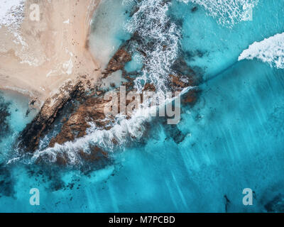 Luftaufnahme von Wellen, Felsen und transparenten Meer. Sommer Meereslandschaft mit Meer, Sandstrand, schöne Wellen, Felsen, blaues Wasser bei Sonnenuntergang. Blick von oben Stockfoto