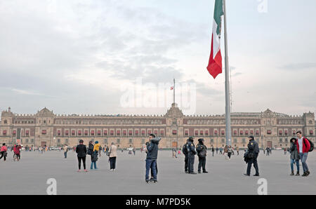 Menschen wandern rund um die Plaza de la Constitucion mit dem Nationalen Palast im Hintergrund der Hauptplatz in Mexiko City, Mexiko. Stockfoto