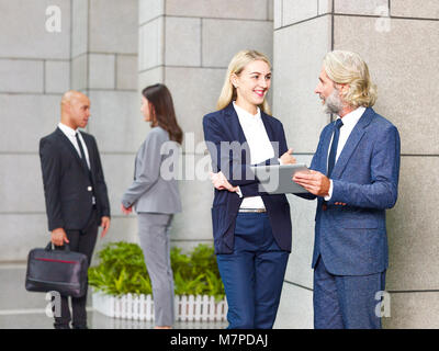 Kaukasische Führungskräfte ständigen Diskussion von mit digitalen Tablet in modernes Gebäude. Stockfoto