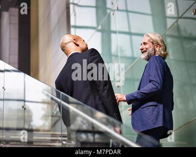 Kaukasische und Latino Führungskräfte reden Chatten während aufsteigende Treppen in modernes Gebäude. Stockfoto