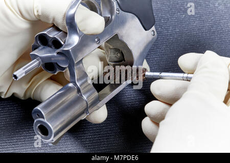 Eine behandschuhte Hand mit einer Drahtbürste eine snubnose Revolver auf einem schwarzen Matte isoliert zu reinigen Stockfoto