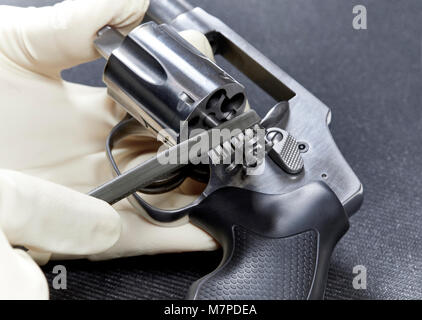 Eine behandschuhte Hand mit einem Borstenpinsel eine snubnose Revolver auf einem schwarzen Matte isoliert zu reinigen Stockfoto