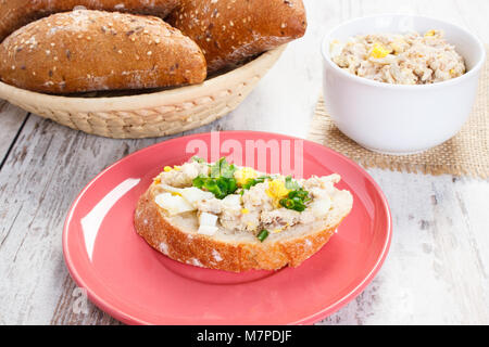 Scheibe knusprigem Baguette mit hausgemachten Makrelen oder Thunfisch, Ei und Schnittlauch, frische Brötchen im Hintergrund Stockfoto