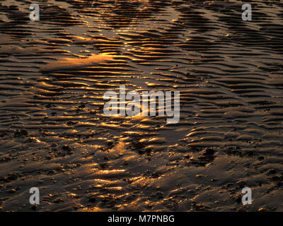 Wellen in den Sand am Meer bei Sonnenuntergang links Stockfoto