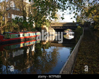 Reflexionen über eine Brücke, eine Barge und Bäume im Wasser der Regents Park Canal im Herbst Stockfoto