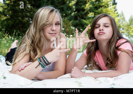 Zwei Mädchen zur Festlegung auf eine Decke, "Frieden" und "Hang Loose" Hand Symbole. Stockfoto