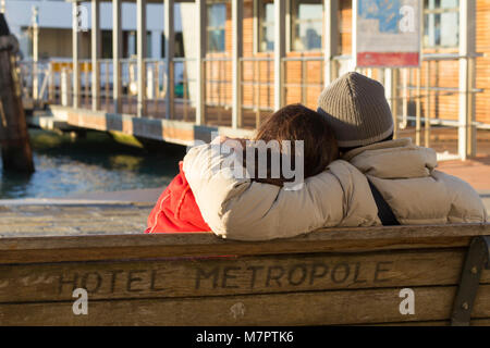 Paar auf einer Bank sitzen außerhalb des Hotel Metropole Riva degli Schiavoni, Venedig mit Blick über das Becken von San Marco. Stockfoto