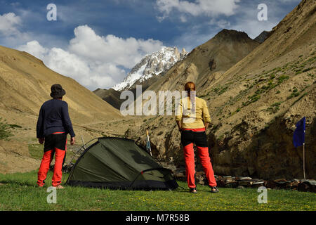 Paar Touristen vor dem Zelt stehen auf dem Trekking in Ladakh, mit Blick auf die verschneiten Gipfel. Diese Region ist ein Zweck der Motorrad Stockfoto