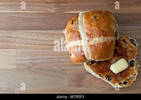 Hot Cross Brötchen mit schmelzender Butter auf Holz- Oberfläche geröstet Stockfoto