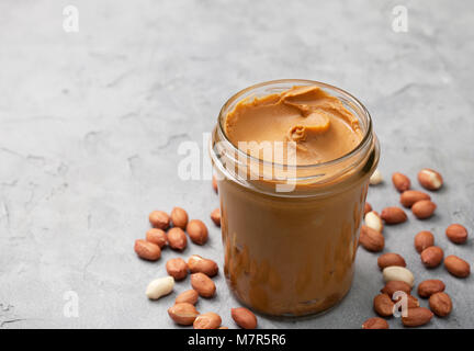 Erdnussbutter im Glas, Erdnüsse auf grauem Beton Hintergrund. Stockfoto