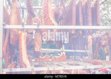 Blick durch Rauch auf gepökeltes Fleisch und Würstchen hängen für Verkauf an einen Flohmarkt. Stockfoto