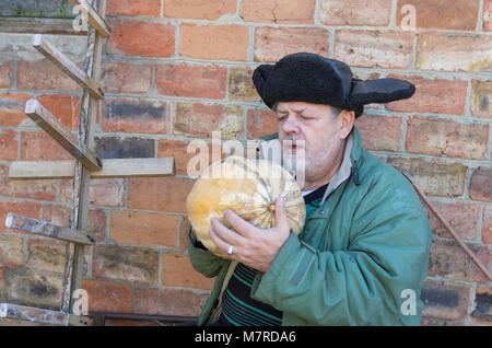 Outdoor Portrait eines bärtigen ukrainischen Bauern mit Kürbis gegen Mauer sitzen Stockfoto