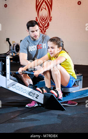 Ein junges Mädchen wurde eine Lektion auf einem Rudergerät in ein Fitnessstudio. Stockfoto