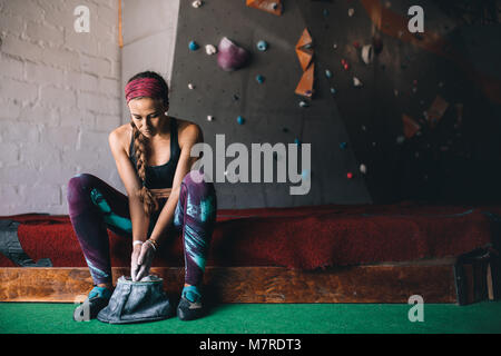 Frau an einem wall Kletterhalle Anwendung magnesium Chalk Pulver auf die Hände aus der Tasche. Künstliche bouldern Wand im Hintergrund. Stockfoto