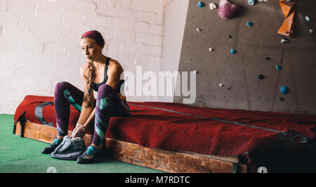 Frau an einem wall Kletterhalle Anwendung magnesium Chalk Pulver auf die Hände aus der Tasche. Künstliche bouldern Wand im Hintergrund. Stockfoto