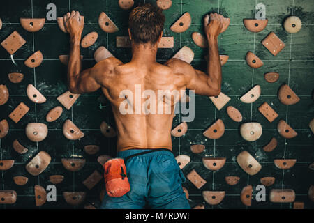 Muskulöse mann Kletterwand im Indoor klettern. Kletterer üben Klettern in einer Kletterhalle. Stockfoto
