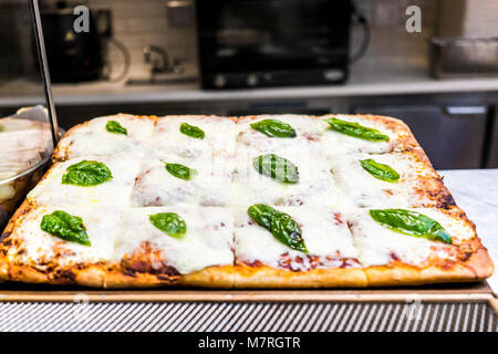 Nahaufnahme von Mozzarella foccacia Brot mit grünen Blätter Basilikum, geschmolzenem Käse Pizza nach dem Backen, goldbraune Kruste auf dem Küchentisch Stockfoto