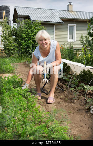 Reife Frau sitzt auf einem Stuhl in seinem Garten und Arbeiten Stockfoto