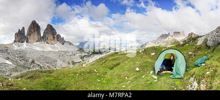 Weibliche Bergsteiger sitzen entspannt im Zelt und lächelt glücklich nach einer Nacht draußen in den Bergen. Great Blick auf die Berge, Tre Cime, drei Zinnen Stockfoto