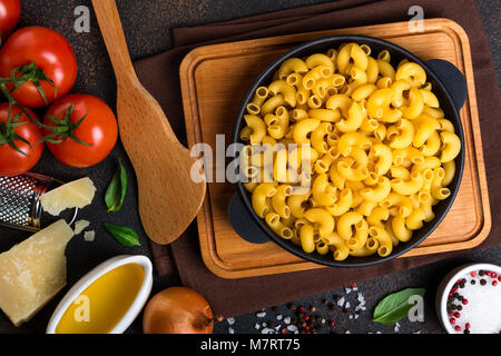 Nudeln und Zutaten zum Kochen auf schwarzem Hintergrund, Ansicht von oben. Italienisches Essen Konzept. Pasta, Tomaten, Basilikum, Gemüse und Gewürze Stockfoto