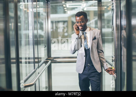 Portrait von afroamerican Geschäftsmann in der modernen Aufzug aus Glas am Telefon sprechen Stockfoto