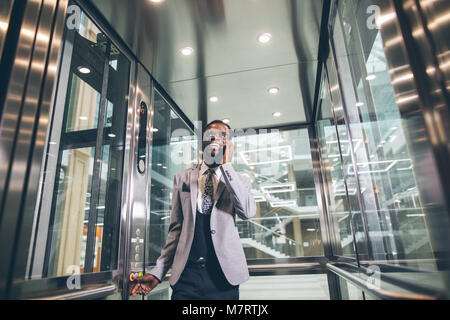 Unternehmer im modernen Aufzug aus Glas sprechen über das Telefon Stockfoto