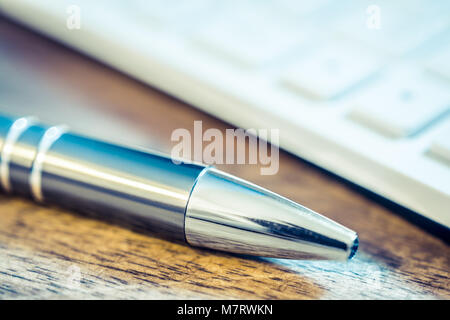 Nahaufnahme von einem Verchromten Bleistift Vor eine weiße Tastatur auf hölzernen Tisch Stockfoto