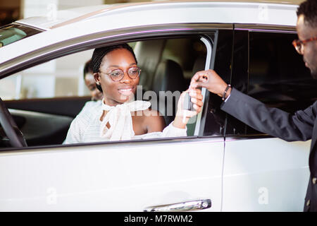 Absatzlage im Autohaus, junge afrikanische Paar erhält die Schlüssel für das neue Auto Stockfoto