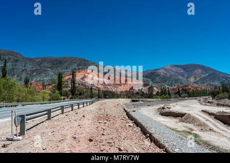 Cerro de Siete colores (Berg der sieben Farben) in Purmamarca, Quebrada de Humahuaca, Weltkulturerbe, Jujuy, Argentinien. Fluss-, Straßen- und guardr Stockfoto