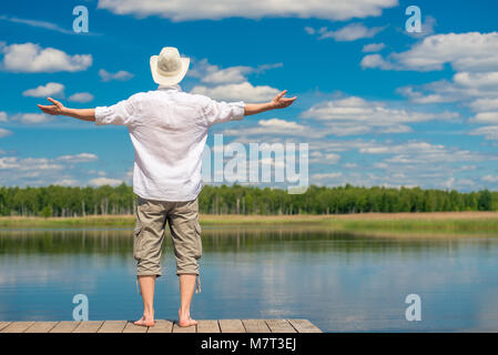 Ein junger Mann im weißen Hemd und Hut genießen Sie die herrliche Natur in der Nähe der See, der Blick von der Rückseite Stockfoto