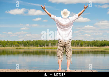 Ein Mann in einem weißen Hemd mit den Armen verteilen sich in den Seiten genießen Sie die herrliche Natur in der Nähe der See, der Blick von der Rückseite Stockfoto