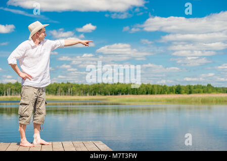 Porträt eines Mannes in voller Länge auf einer hölzernen Pier, zeigt seine Hand zur Seite Stockfoto