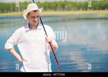 Portrait Of Happy Fischer in einem weißen Hut auf einem See Hintergrund Stockfoto