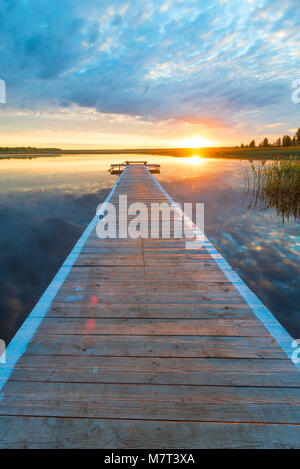 Vertikale Foto von einer schönen Landschaft - eine lange hölzerne Seebrücke und eine untergehende Sonne über einem malerischen See Stockfoto