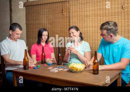 Vier Freunde, die Karten an einem Tisch drinnen sitzen, Bier trinken. Stockfoto