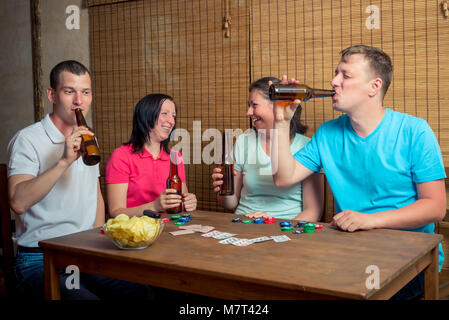 Eine Gesellschaft von Freunden Bier trinken und Karten spielen an einem Tisch drinnen sitzen Stockfoto