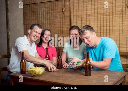 Jung und glücklich vier Freunde beim Poker Spielen am Tisch und Bier trinken. Stockfoto