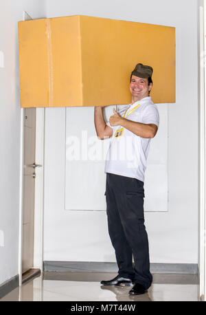 Der Postbote trägt ein grosses Paket auf seinen Schultern. Der E-Mail-Dienst trägt eine große Lieferung in die Wohnung. Stockfoto