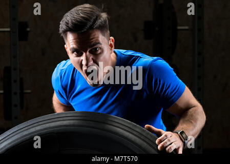 Nahaufnahme Porträt einer schreienden Sportler, Bodybuilder Heben einer schweren großen Rad Stockfoto