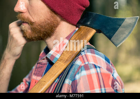 Ein Förster mit einem roten Bart mit einer Axt auf die Schulter Spaziergänge durch den Wald, eine Nahaufnahme Porträt Stockfoto