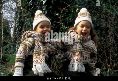 Zwei glückliche kleine Schwestern im Winter woollies sitzen auf Zaun in der Landschaft Stockfoto