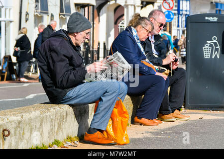 Honiton, Devon, Großbritannien. 13. März 2018. UK Wetter. Ein Mann eine Zeitung lesen direkt am Meer am Badeort Sidmouth in Devon, an einem warmen, sonnigen Frühling Nachmittag. Foto: Graham Jagd-/Alamy Leben Nachrichten. Stockfoto