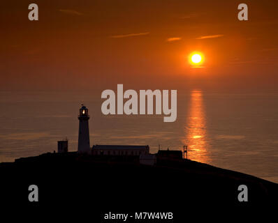 South Stack lighthouse at Sunset, Anglesey, Nordwales mit Sonne auf einem ruhigen Meer Stockfoto