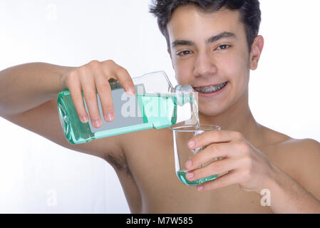 Cute Teenager mit weißem Hintergrund, das Tragen von Zahnspangen auf seine Zähne. Ein Desinfektionsmittel Mundwasser im Rachen Spray. Portrait im zweiten Stock verwischt. Stockfoto